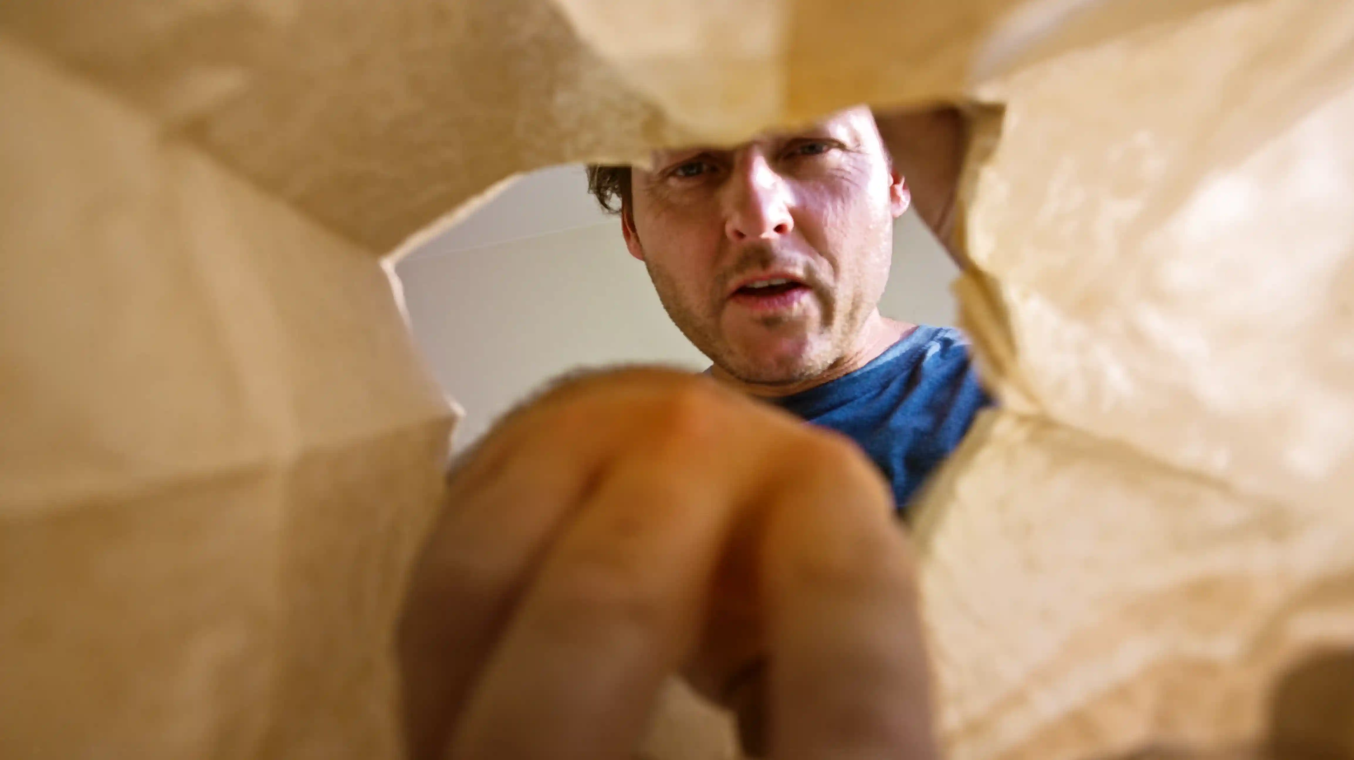 Man reaching into a paper bag viewed from inside the bag.