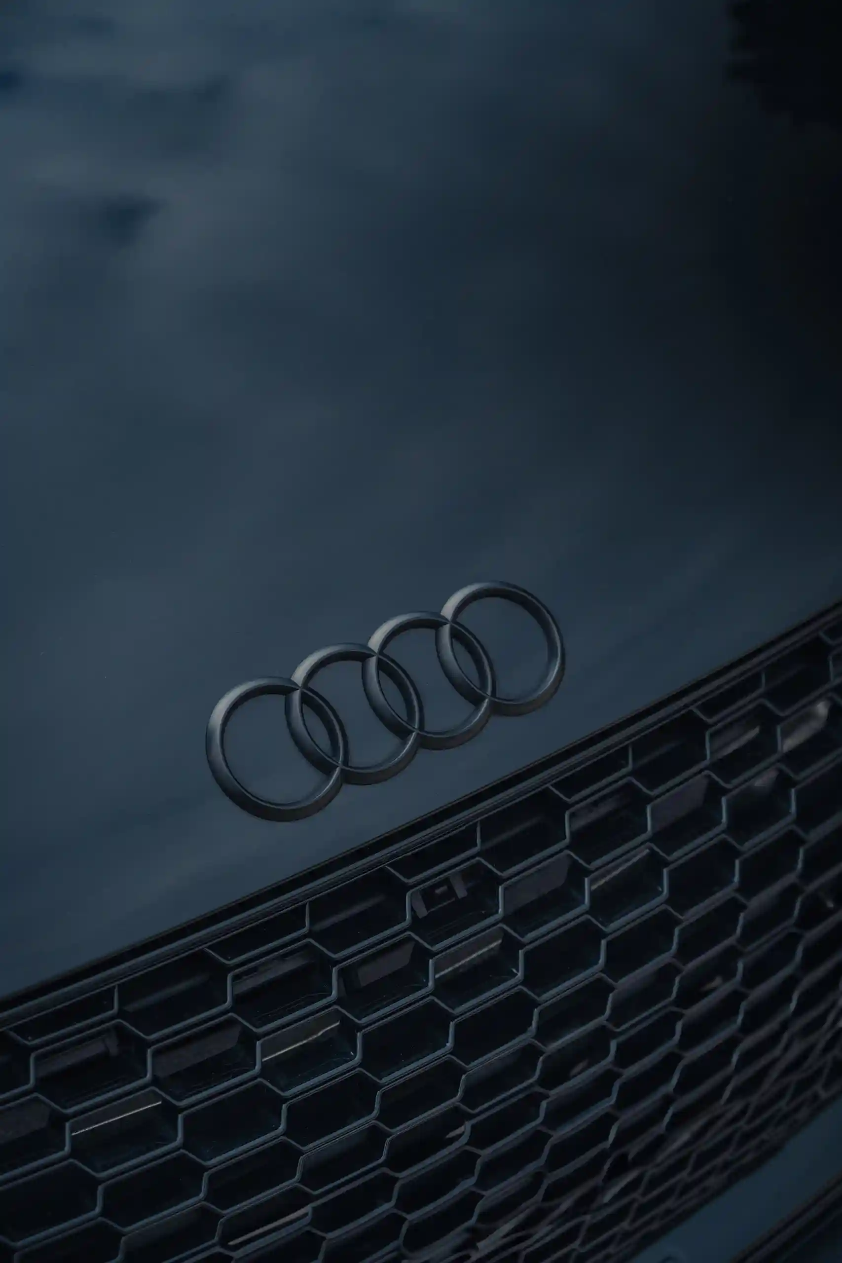 Close-up of a black Audi car hood and front grille featuring the Audi four-ring logo.