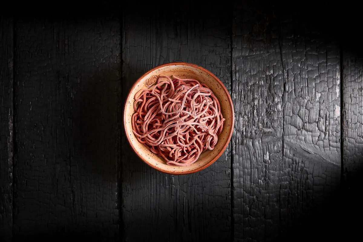 Bowl of uncooked pink noodles on a dark textured wooden surface.