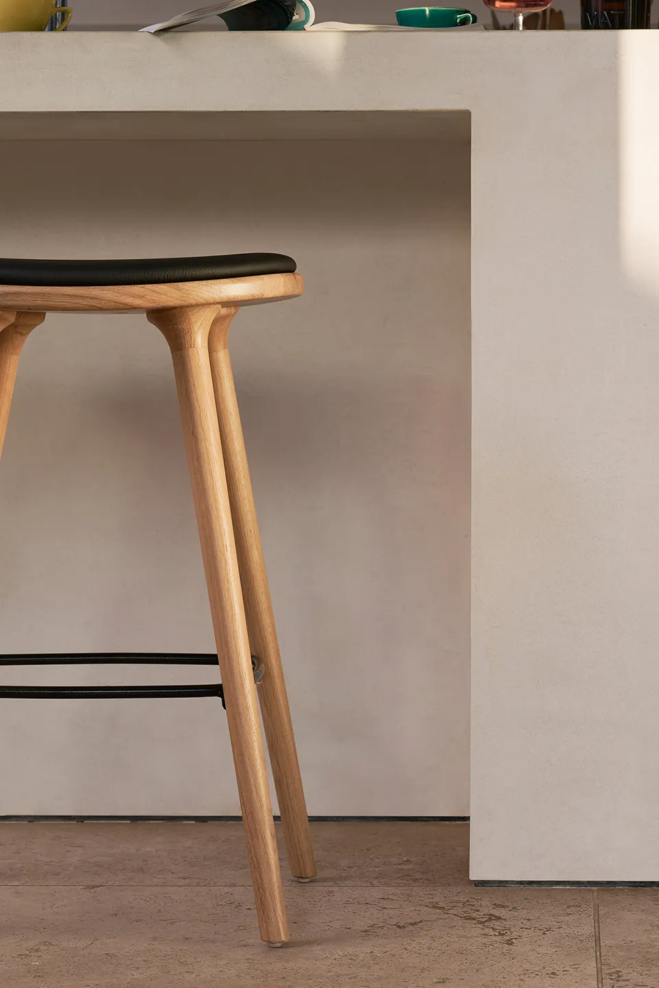Close-up of a wooden stool with a black cushioned seat placed next to a beige counter.