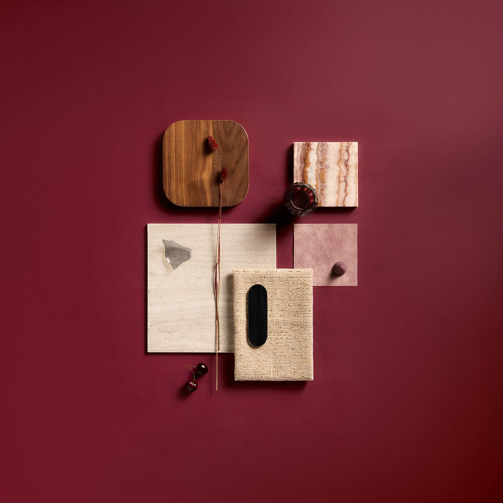 Flat lay of material samples including wood, stone, fabric, and small decorative items on a deep red background.
