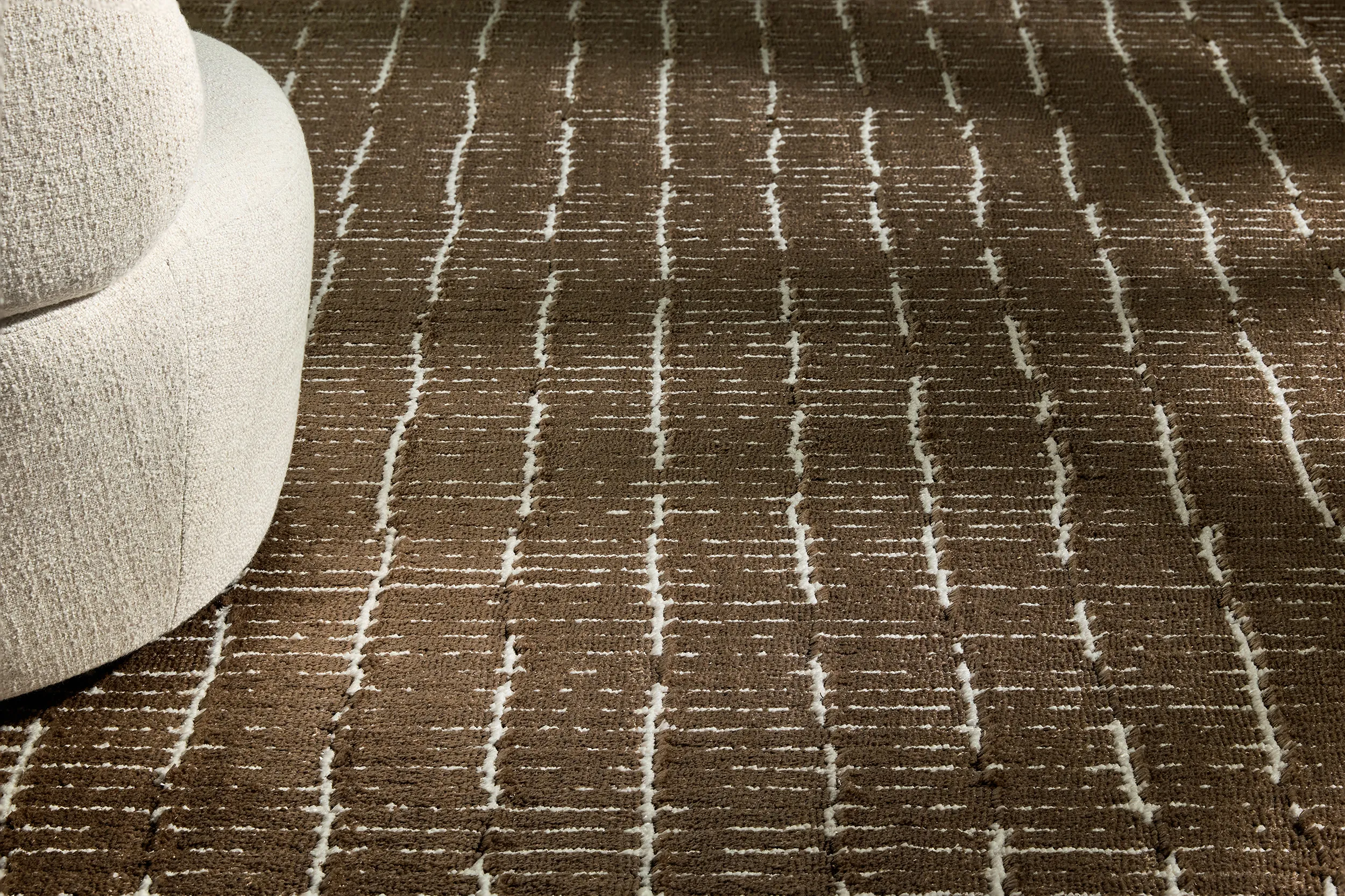 Close-up of a textured brown rug with irregular white linear patterns next to a curved beige upholstered sofa.