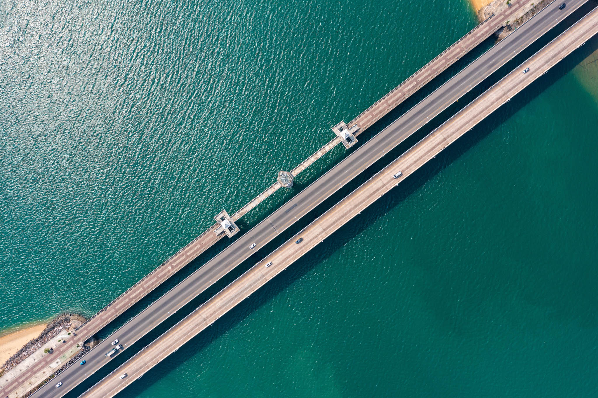 Cras driving across a bridge over a clear body of water.