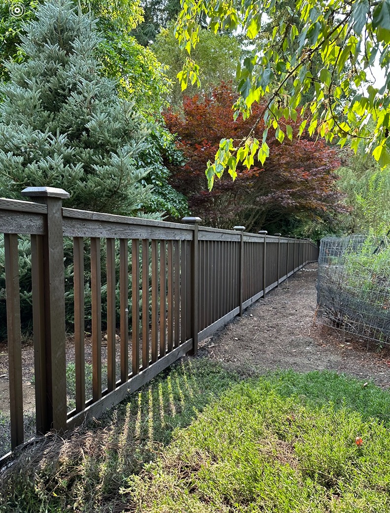 dark brown wooden fence with vertical slats and decorative post caps runs alongside a garden