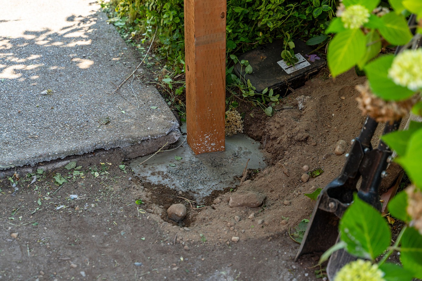 wooden fence post is newly set in concrete at the edge of a garden bed
