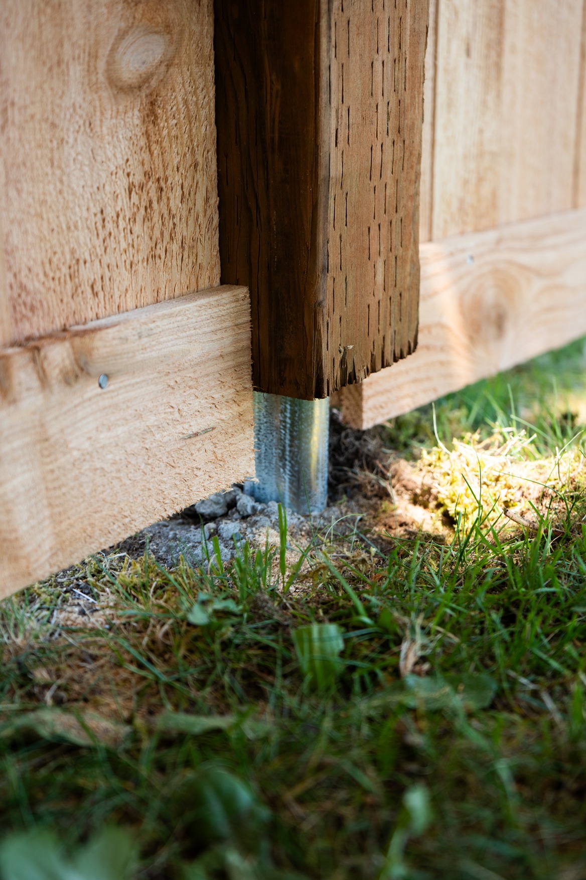 Close-up of a wooden fence post secured with a metal post anchor set in concrete