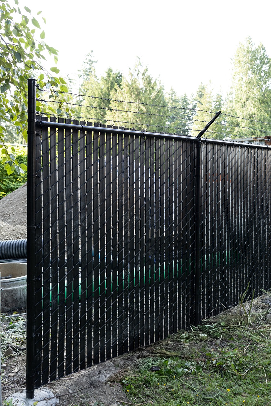 Black chain-link fence with vertical privacy slats and barbed wire