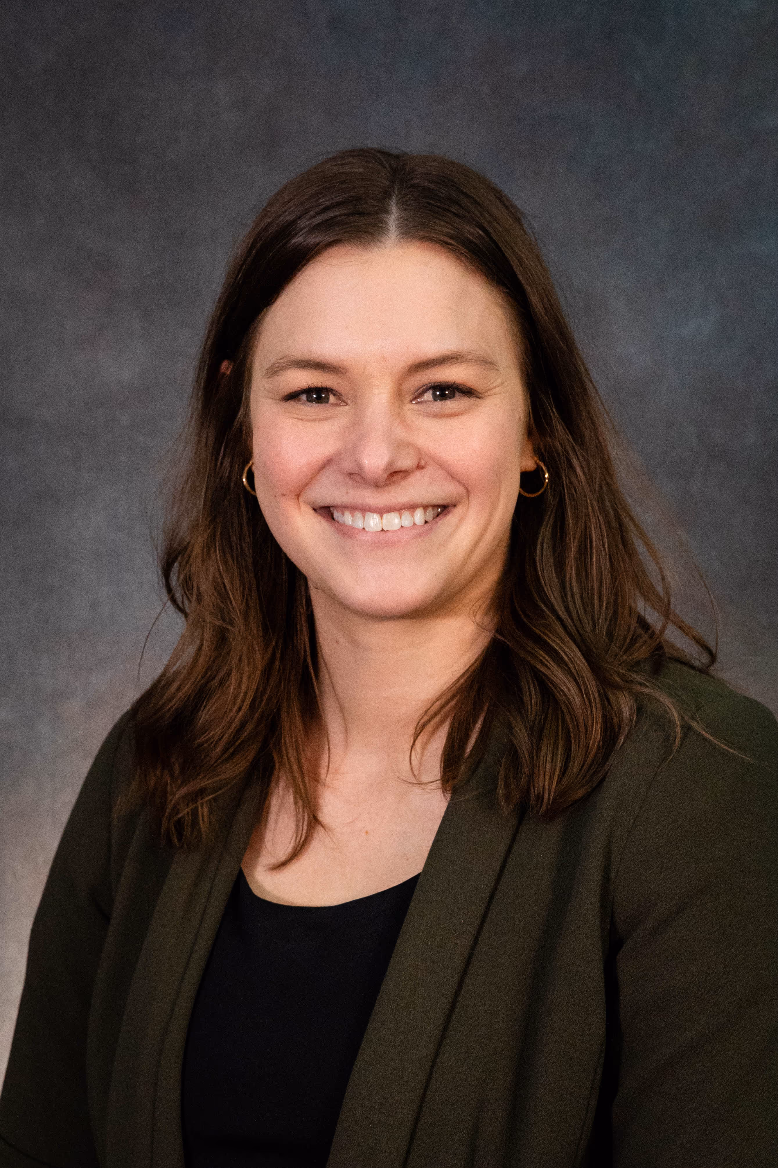 A professional headshot of a woman with brown shoulder length hair,