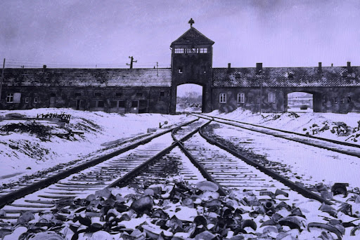 The main gatehouse at Auschwitz II-Birkenau in winter, with railway tracks running through the archway