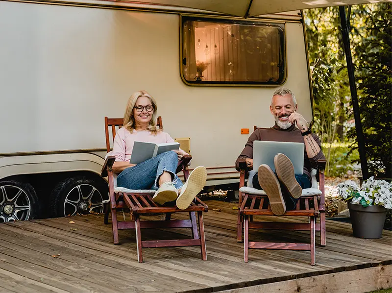 Man zit relaxed op een houten veranda voor zijn camper en stelt op zijn laptop een USB-paneel samen in de VOLUX configurator.