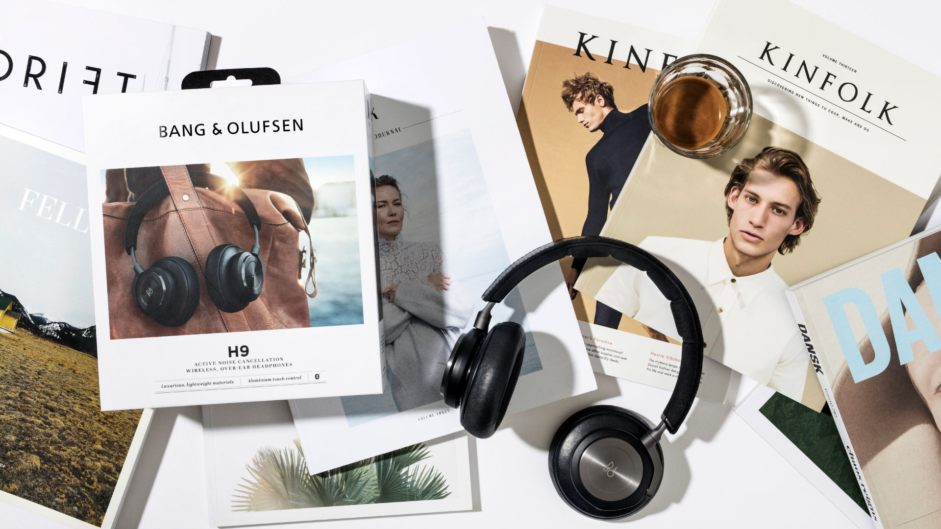 Flat lay photograph of Bang & Olufsen H9 headphone packaging surrounded by lifestyle magazines like Kinfolk and DANSK, with the headphones placed beside the box. Styled with natural light and a coffee glass, the scene captures a premium Scandinavian lifestyle. Created by N96, a Copenhagen-based design studio working at the intersection of strategy, branding, and identity.