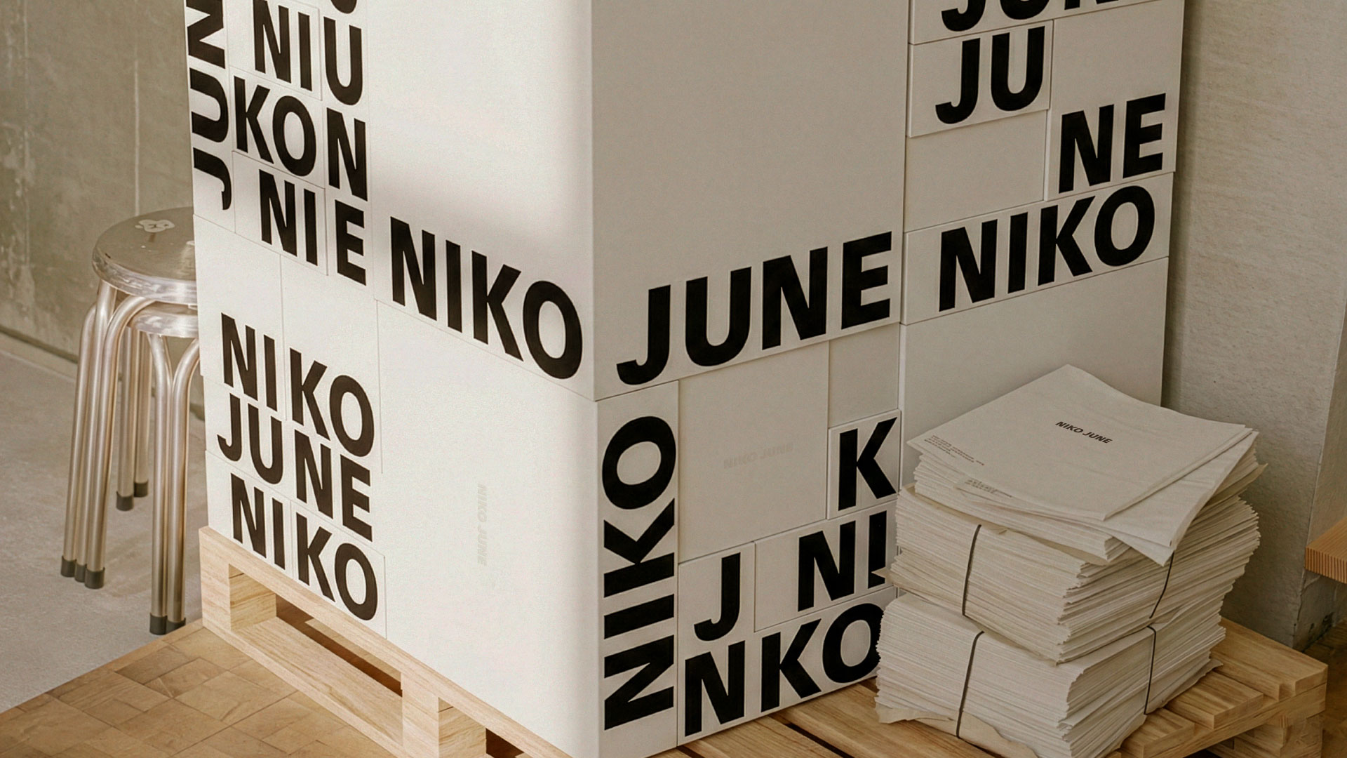 Stack of minimalist white branded boxes featuring bold black typography spelling “NIKO JUNE,” designed as part of a retail installation for Copenhagen-based art and design brand NIKO JUNE. Displayed on wooden pallets alongside bundled printed materials, the setup reflects a strong industrial aesthetic with a clean, modern edge. This brand identity and packaging concept was developed by N96, a Copenhagen-based design and strategy studio, known for crafting visionary consumer brands that connect on a personal level. Perfectly suited for clients searching for Scandinavian packaging design, modern brand identity, retail experience design, and visual storytelling.