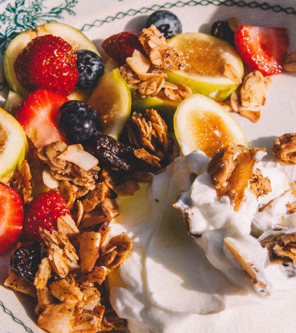 Close-up of Jamie's Farm granola served with fresh strawberries, blueberries, green apple slices and yogurt on a white plate