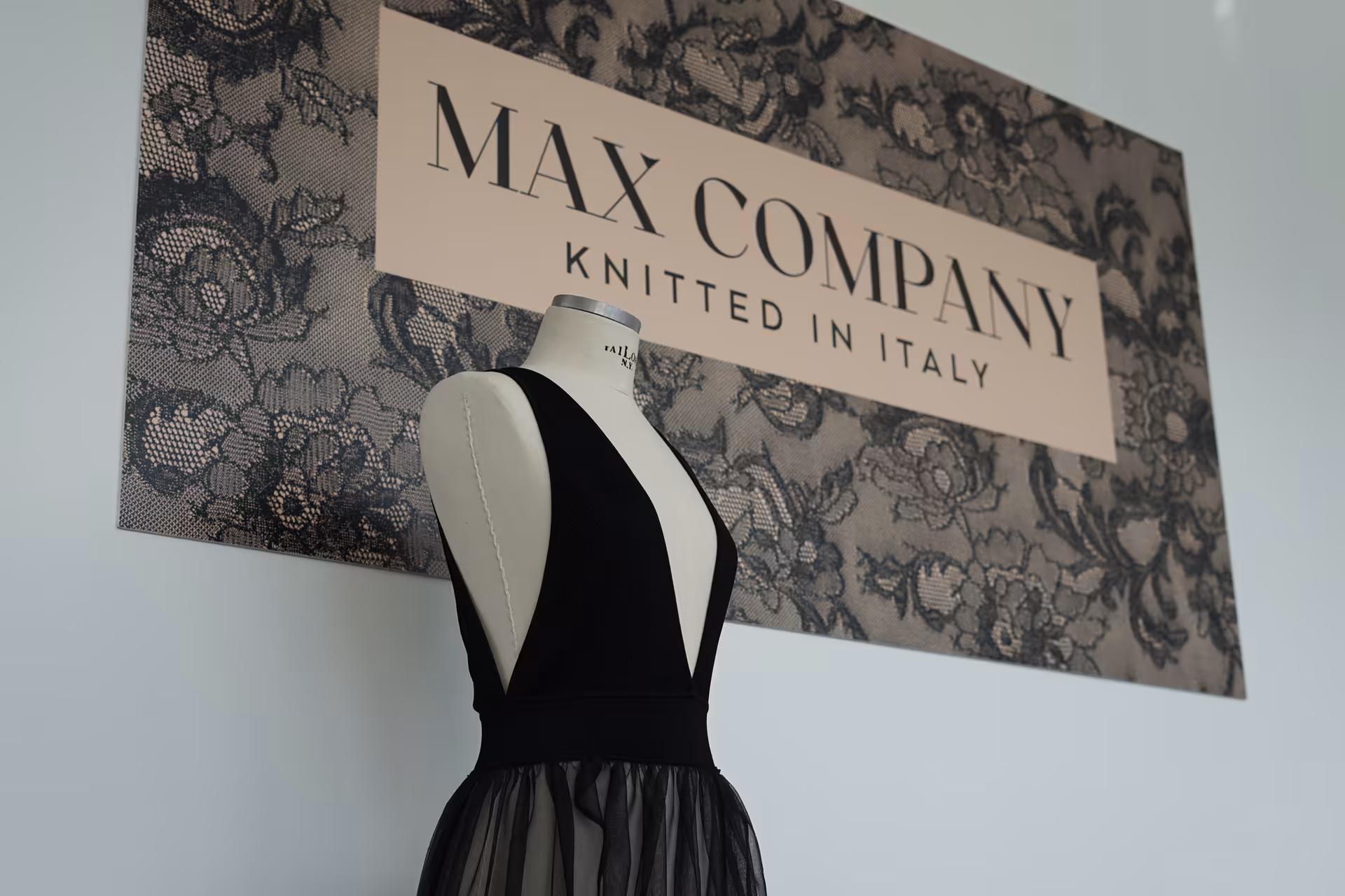 Manichino con abito in maglia davanti al logo Max Company Knitted in Italy – simbolo dell’eccellenza italiana nella produzione di maglieria di alta gamma.