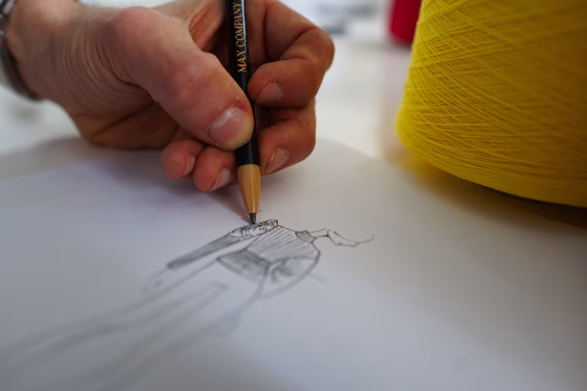 Mano che disegna uno schizzo di capo in maglia con matita Max Company – ideazione e sviluppo creativo per collezioni di maglieria Made in Italy.