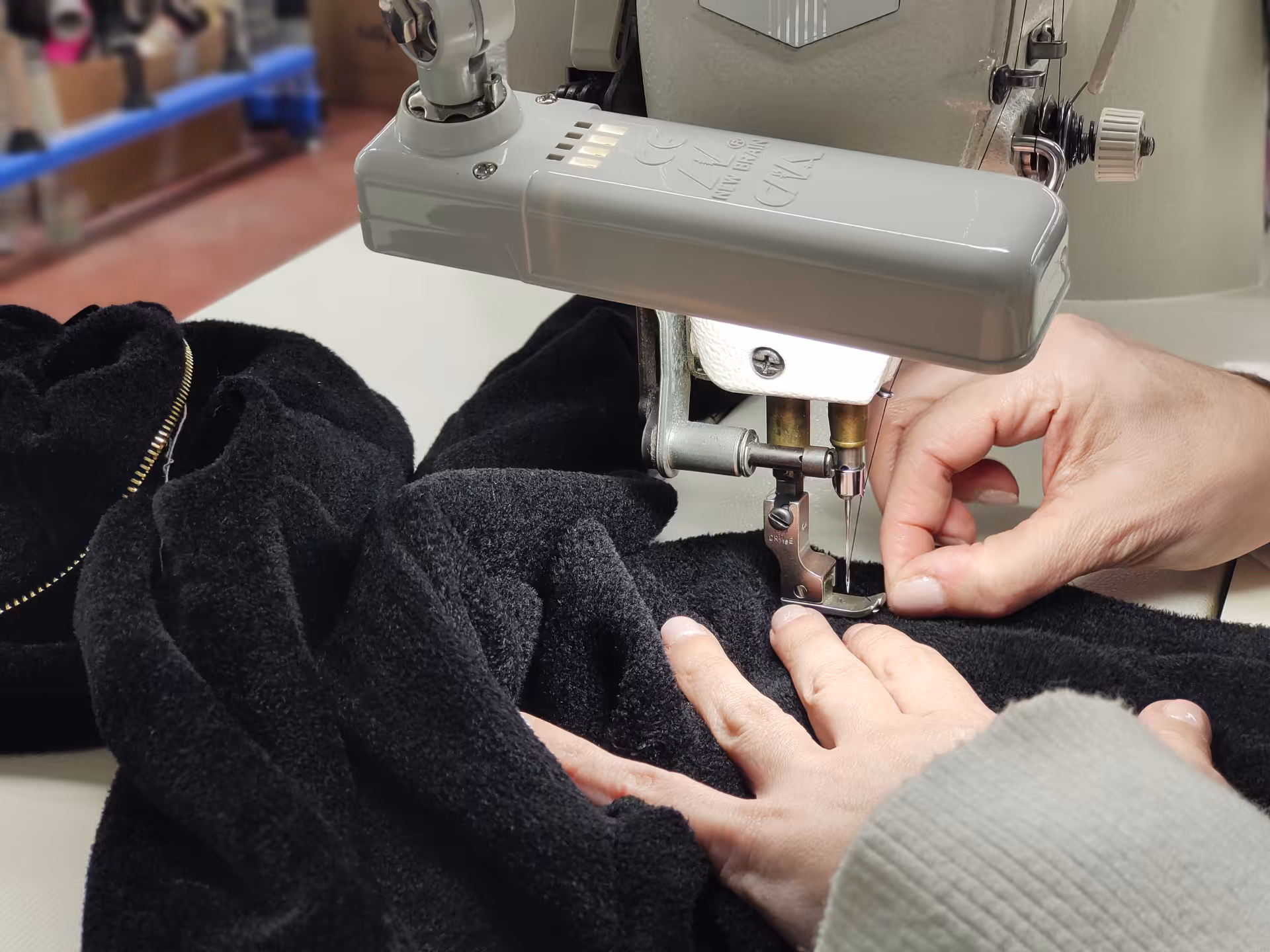 Cucitura di un capo in maglia nera su macchina da cucire industriale – fase di confezione artigianale all’interno del maglificio Max Company.