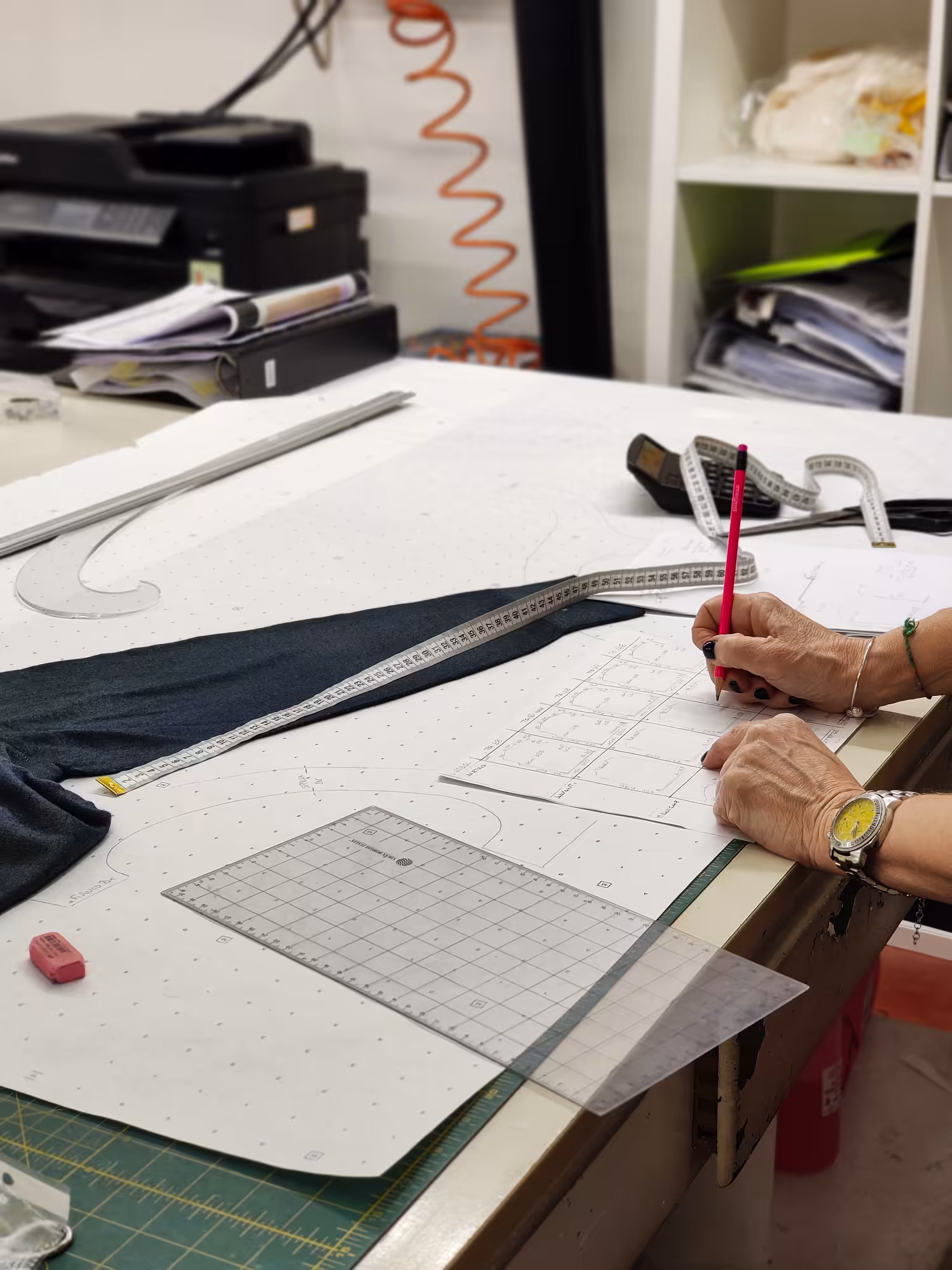 Mani che controllano le misure di un capo prototipo in maglia su scheda taglie – sviluppo prodotto Max Company, Made in Italy.