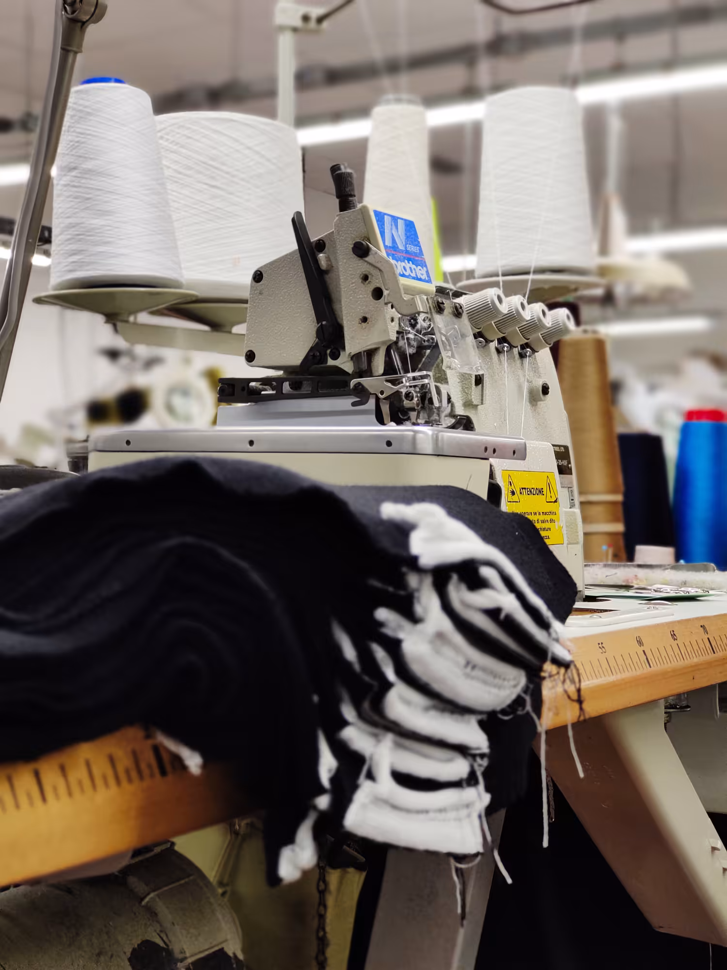 Macchina tagliacuci industriale con rocche di filato bianco – reparto confezione maglieria Max Company.