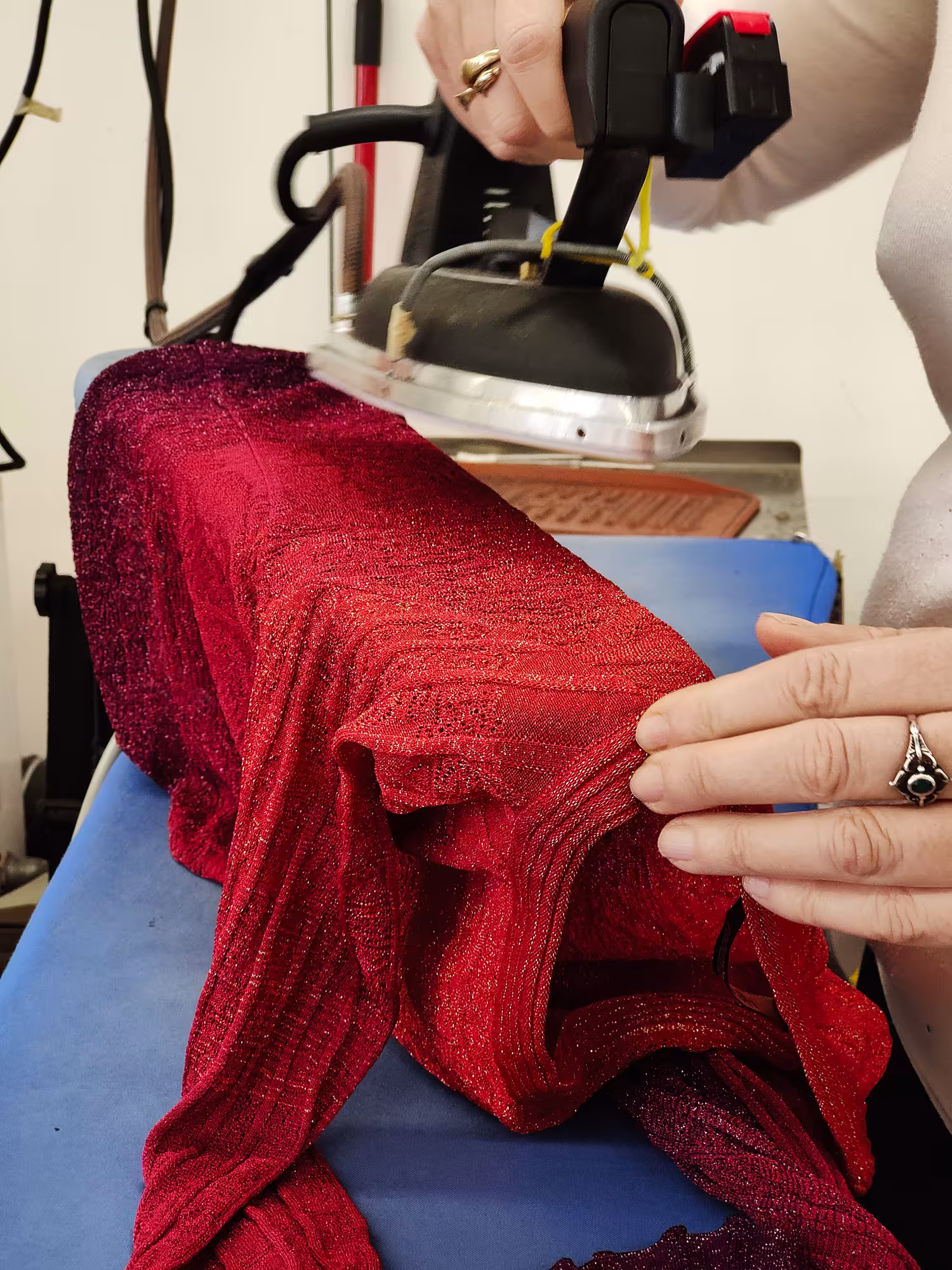 Stiratura manuale di un capo in maglia rossa lurex – fase di finitura e controllo qualità nella produzione Made in Italy di Max Company.