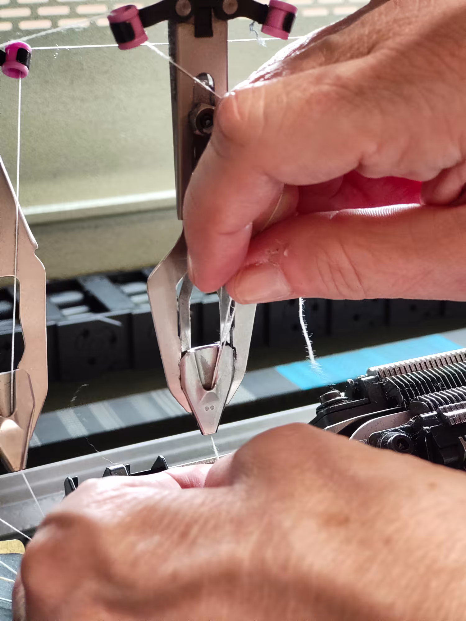 Mano che inserisce il filato nella guida fili di una macchina Shima Seiki – preparazione alla tessitura di maglieria fine Made in Italy.