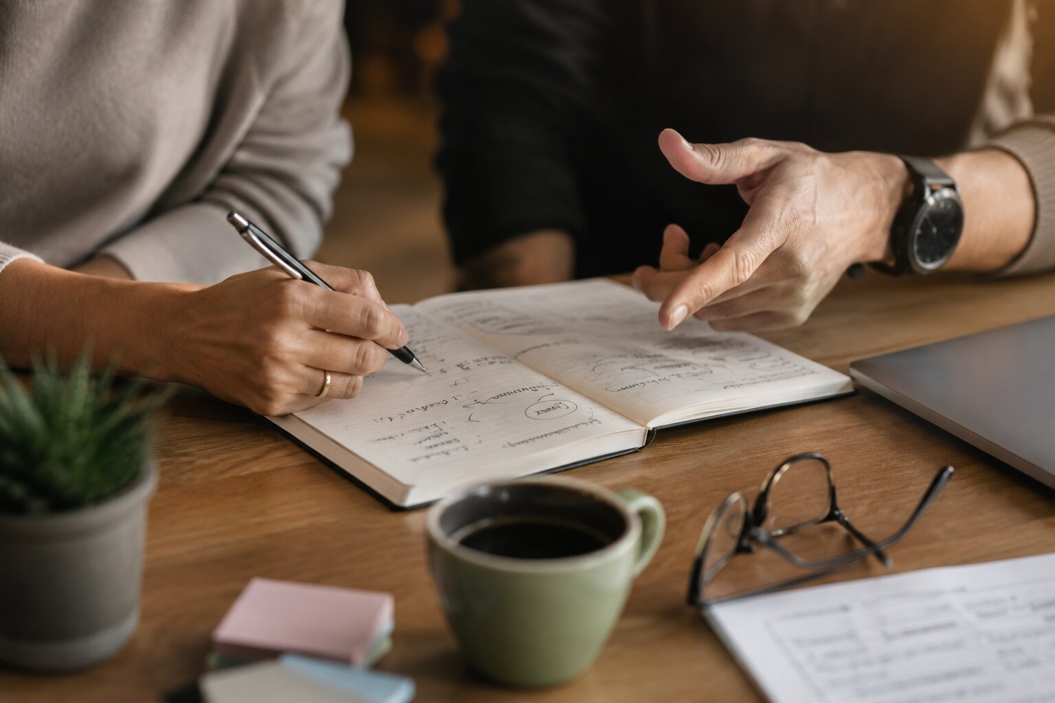 Close-up entrepreneur coaching session with hands, notebook, goal planning, and focused business strategy.