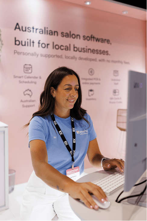 Smiling Weeha team member in a blue Weeha shirt working at a computer on the Weeha stand