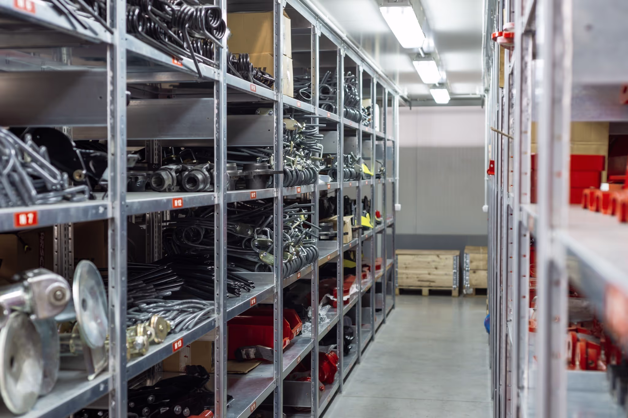 Narrow aisle between metal shelving units filled with organised industrial parts and components in a warehouse or storage facility