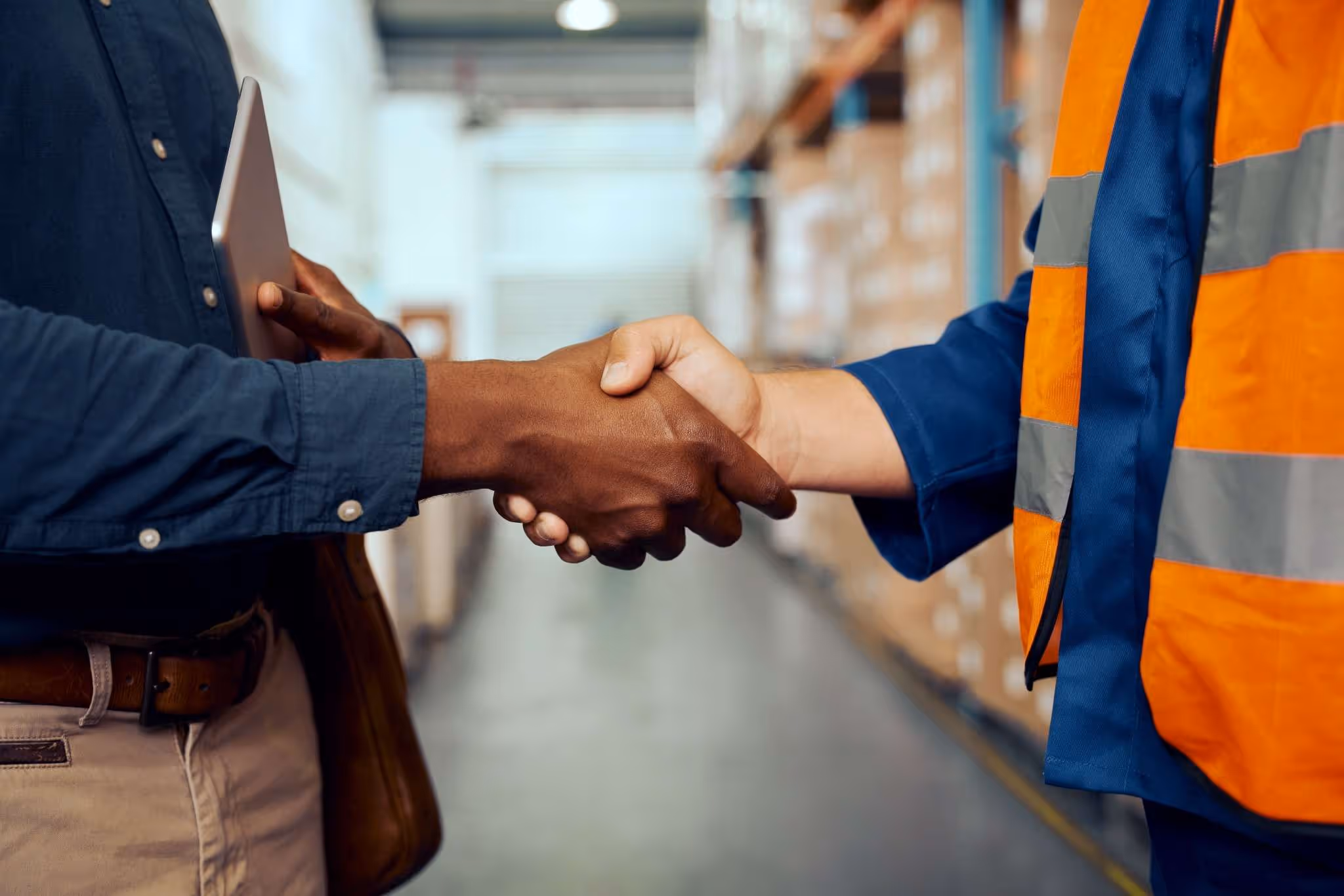 Engineer or industrial warehouse worker shaking hands with man in a suit jacket