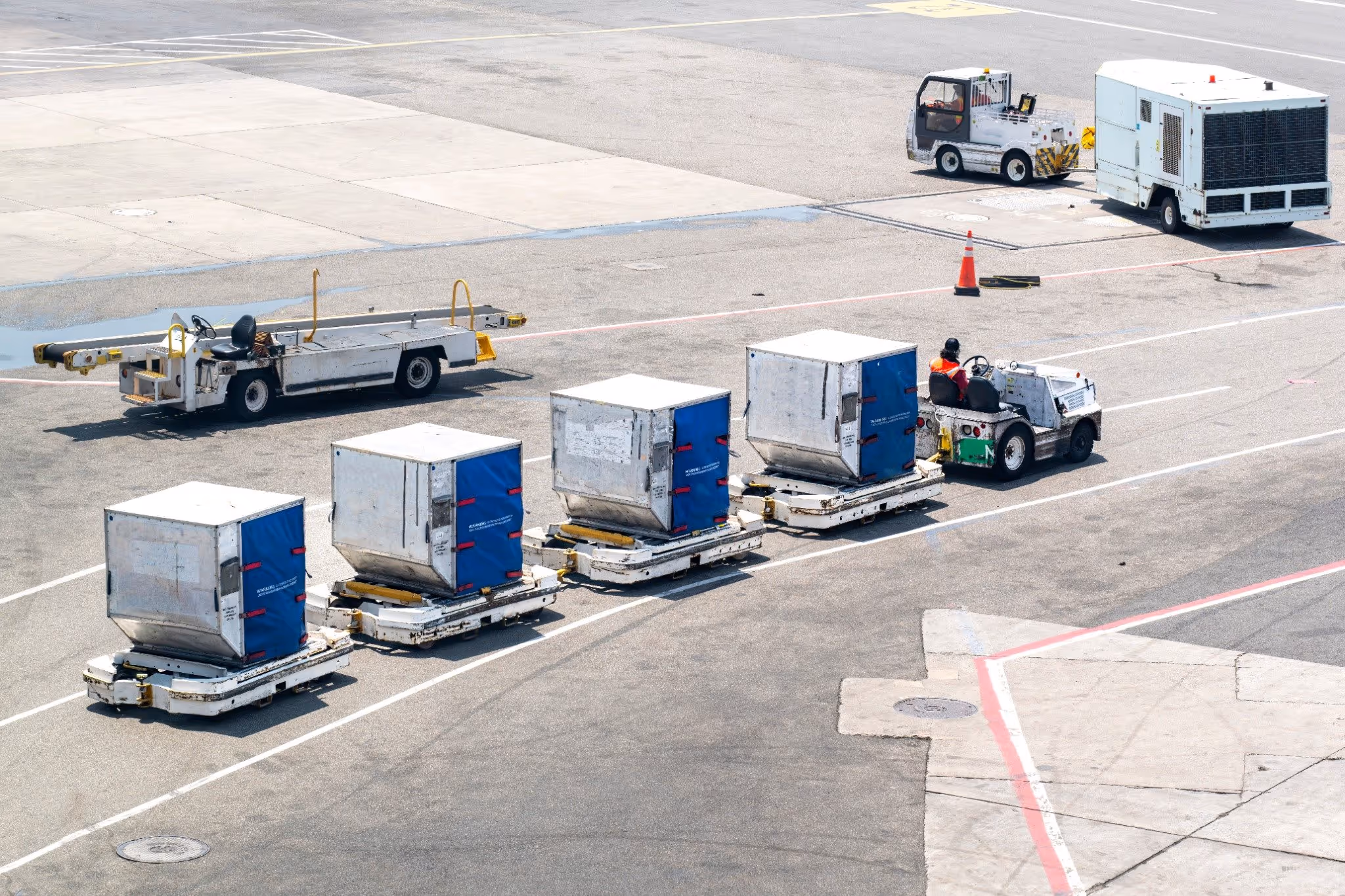High-angle view of airport service road with baggage vehicles, belt loader, and mobile generator.