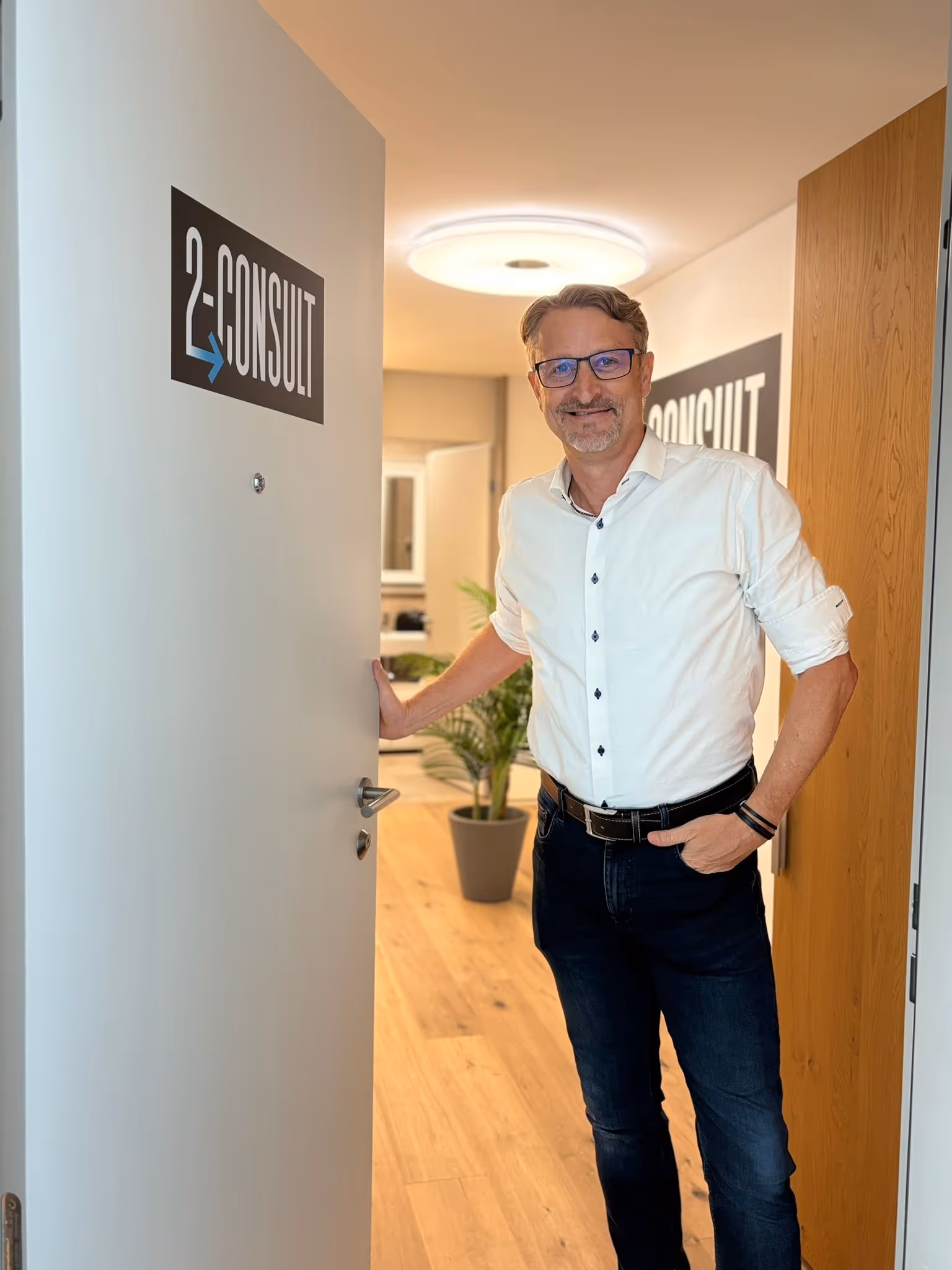 André Burkhart begrüßt im Türrahmen des 2-Consult Büros