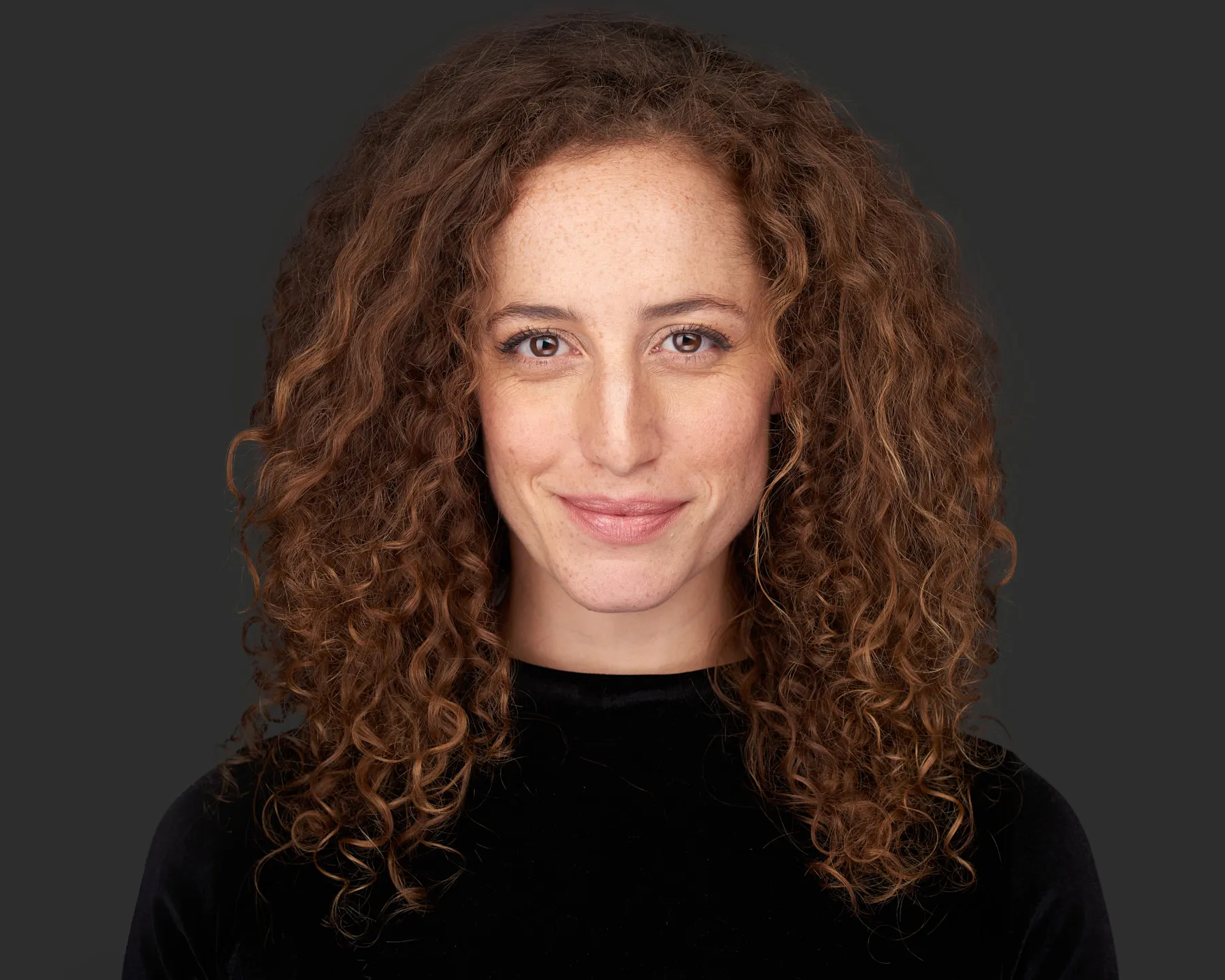 צילום תדמית מקצועי של אישה עם שיער מתולתל על רקע כהה בסטודיו