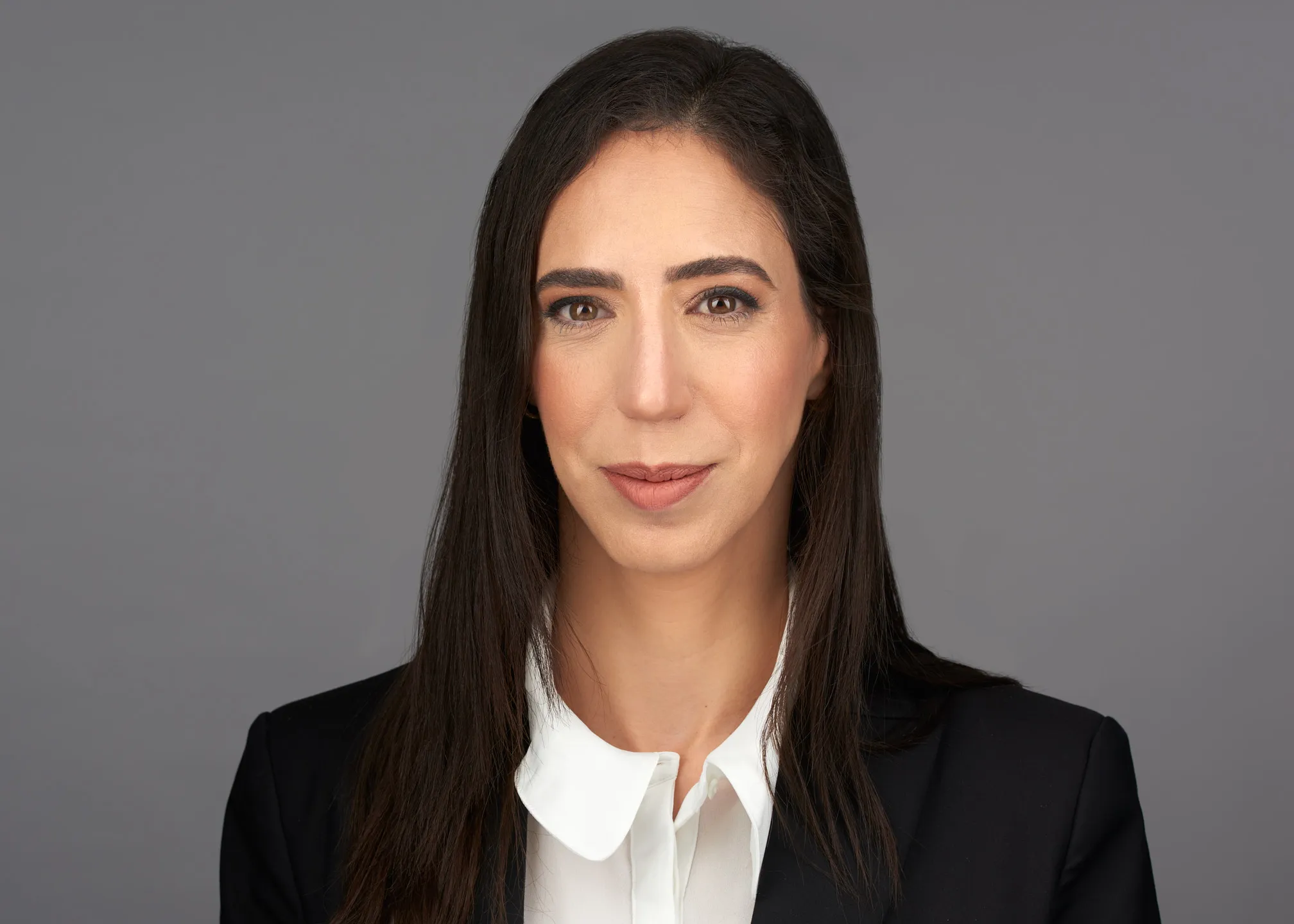 צילום תדמית לעורכת דין בבלייזר שחור וחולצה לבנה על רקע אפור