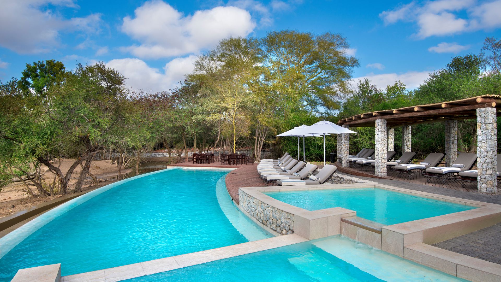 Large swimming pool surrounded by trees and garden, perfect for relaxing between safaris.
