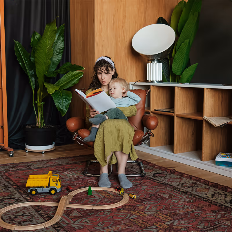 Woman sitting in a brown chair reading a book to a child. Clean Slate Clinic client. 