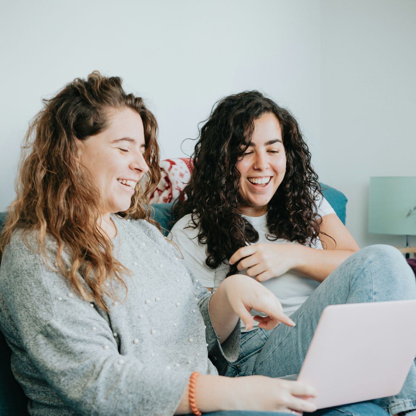 Two women smiling together on a sofa at home
