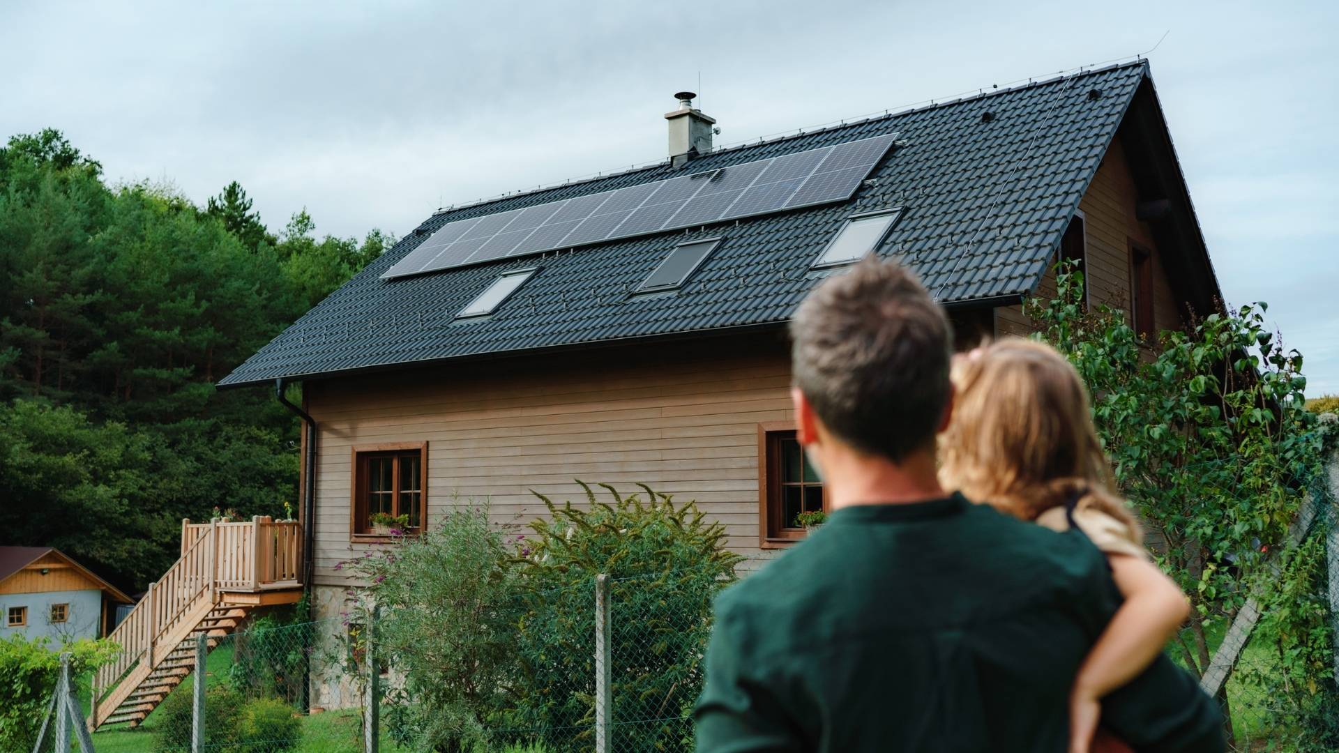 Wohnhaus mit moderner Solaranlage in Köln – Familie betrachtet eine installierte PV-Anlage auf dem Hausdach im Grünen.