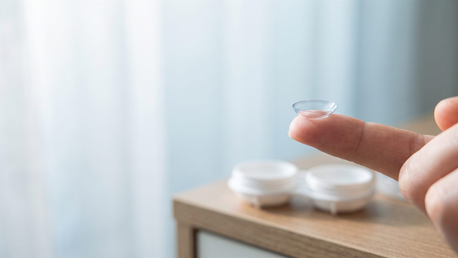 A small rigid orthokeratology contact lens on a fingertip in soft morning light.