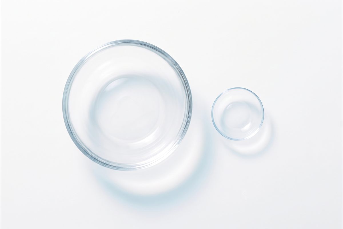 A large scleral contact lens beside a much smaller standard soft contact lens on a white surface, showing the difference in diameter.