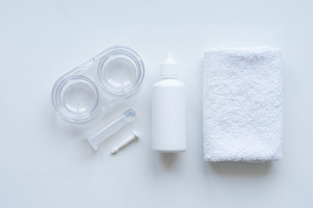 Scleral lens care items on a clean counter: a deep-well lens case, an insertion plunger, a removal plunger and a bottle of saline.