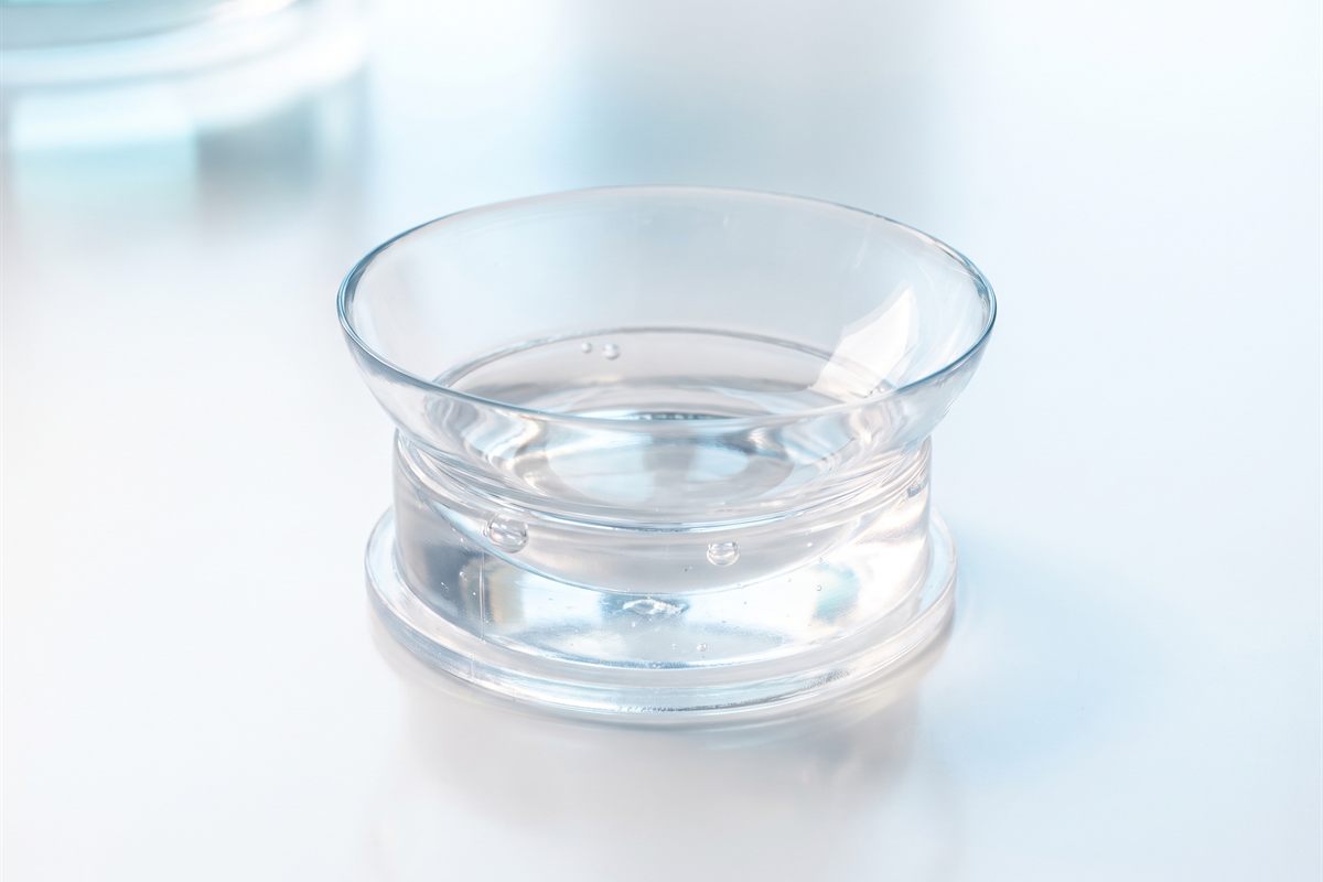 A large-diameter scleral contact lens resting in a clear insertion plunger filled with saline, showing its wide bowl-shaped profile.