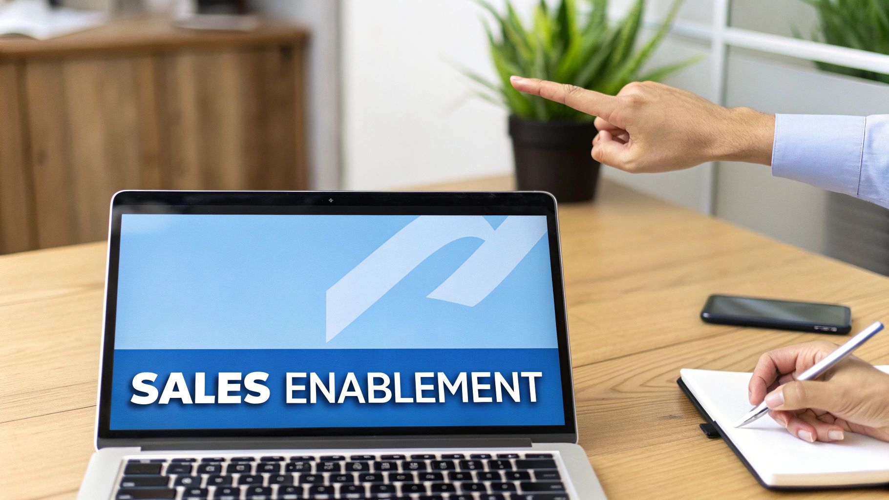 A laptop displays 'SALES ENABLEMENT' while a hand points and another writes notes.