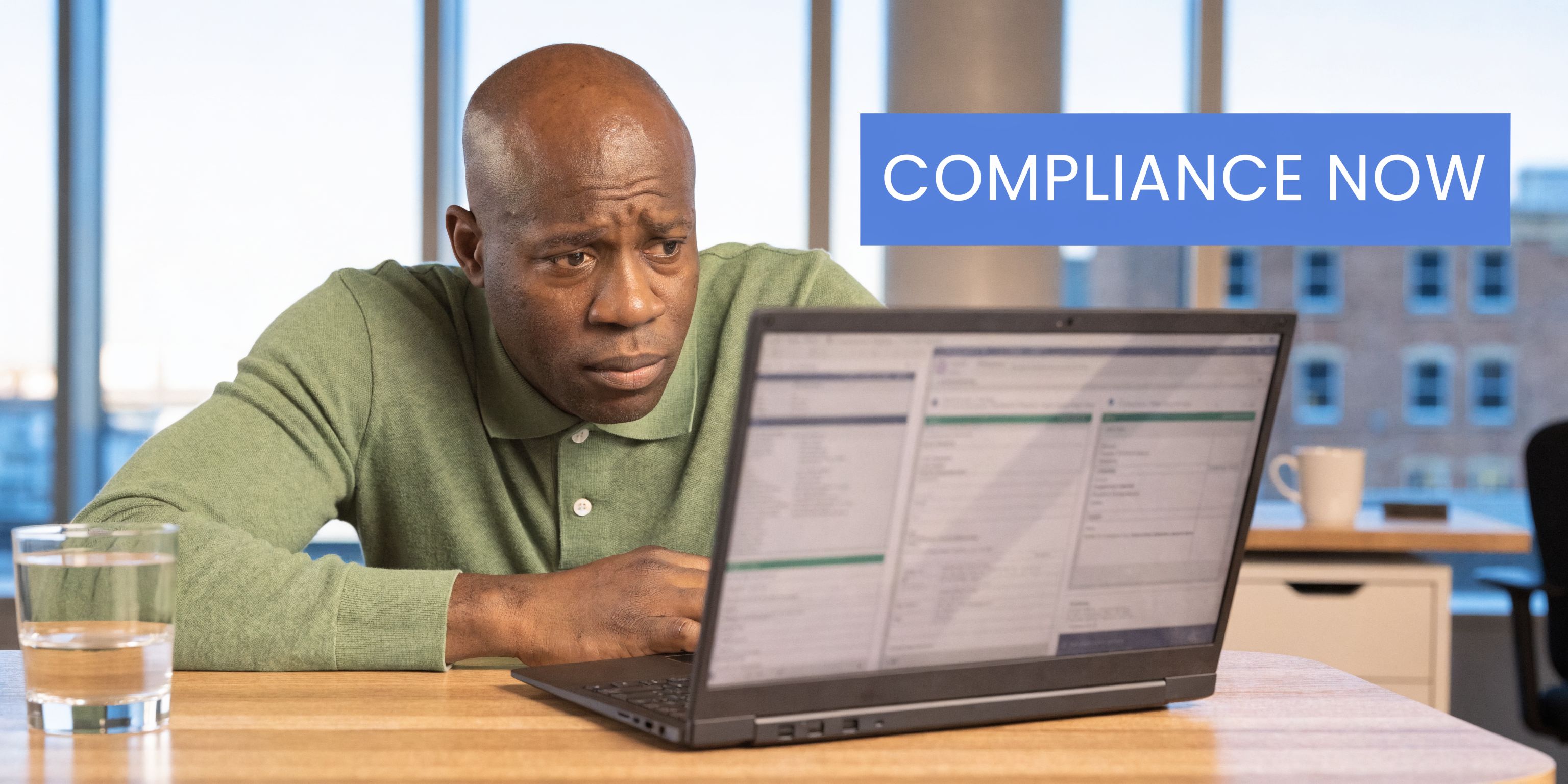 A focused man sitting at a desk and working on a laptop in a modern office.