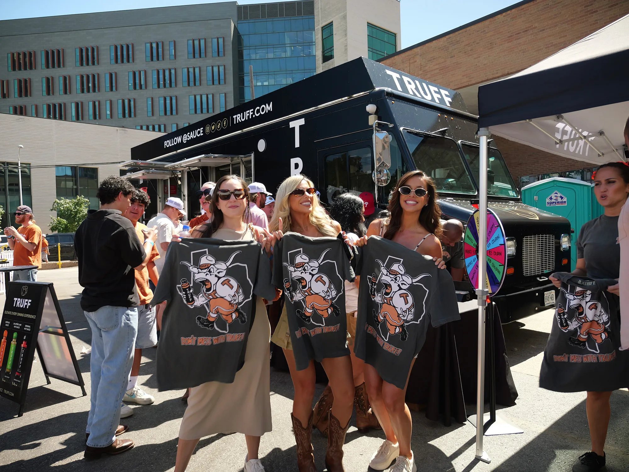 Guests holding branded T-shirts in front of a TRUFF activation with a prize wheel