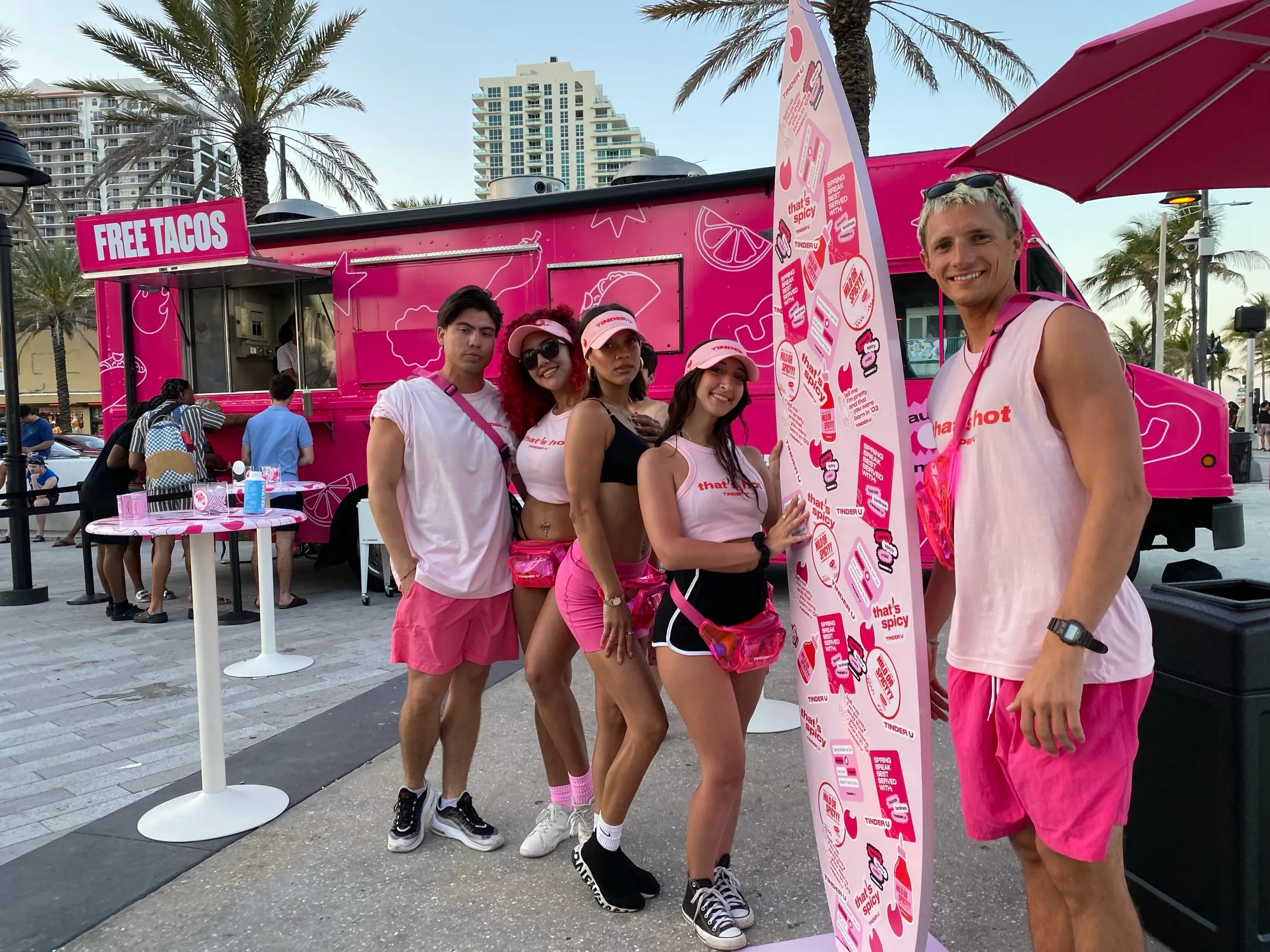 Event staff in matching pink outfits in front of a pink activation trailer offering free tacos