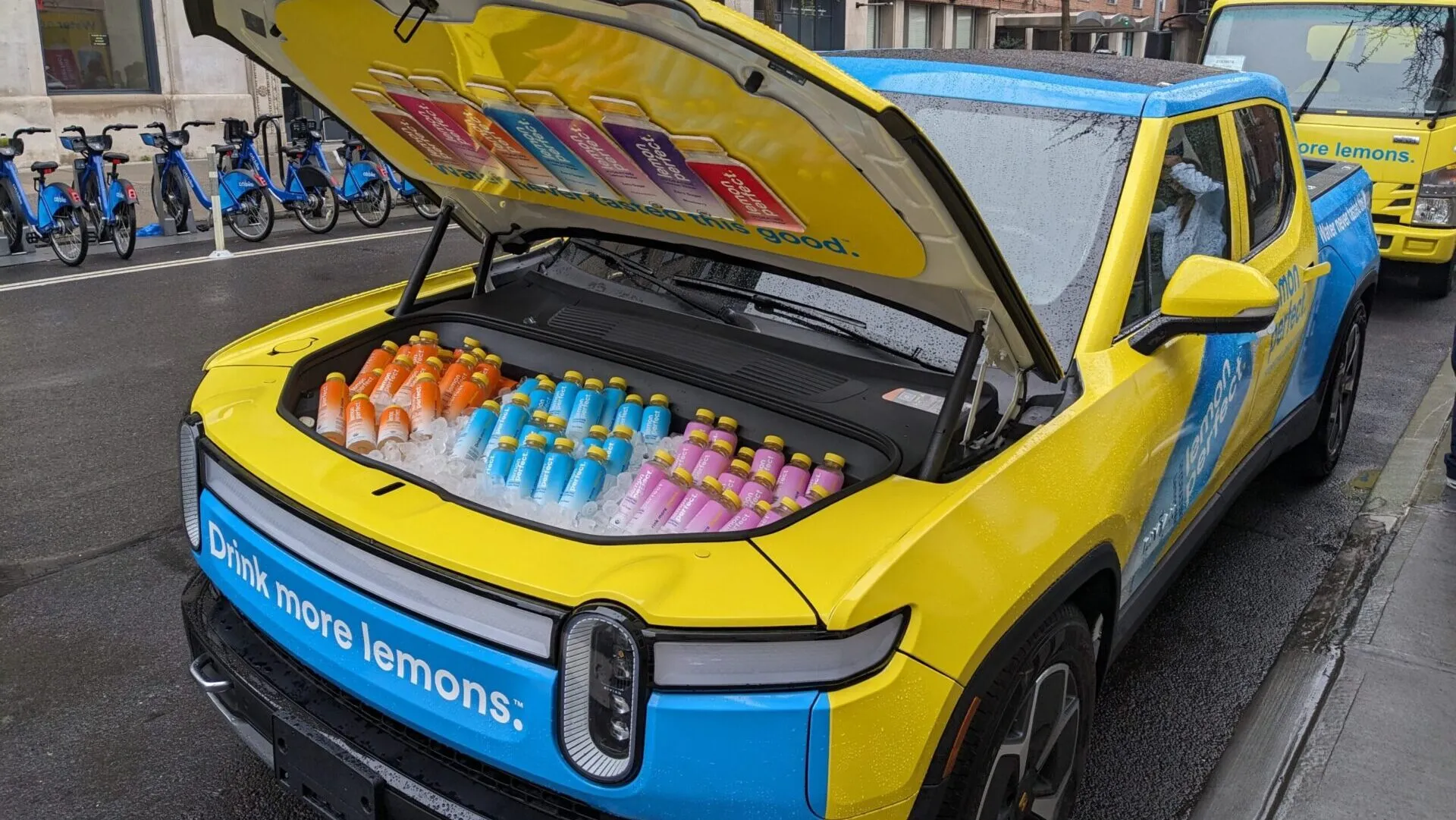 Yellow and blue branded electric pickup with its front trunk open and stocked with bottled drinks