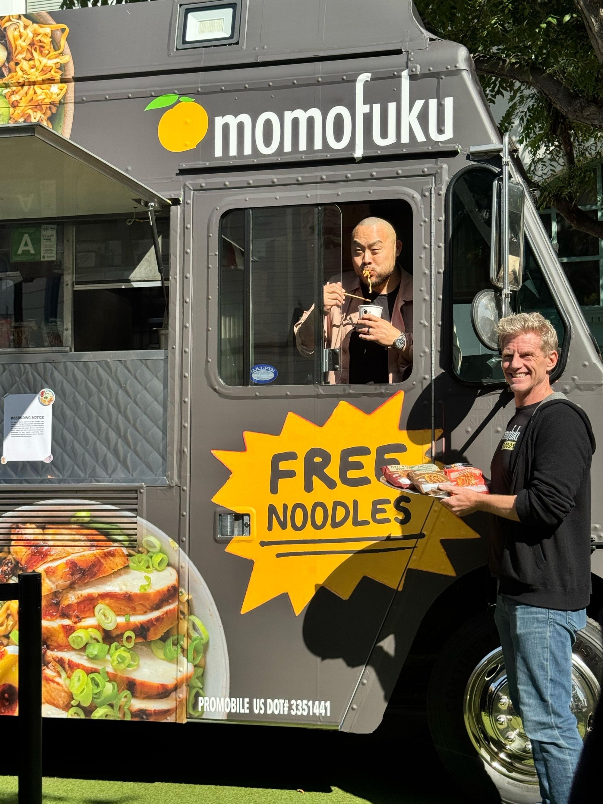 Momofuku food truck window with a free noodles starburst sign and staff serving a guest