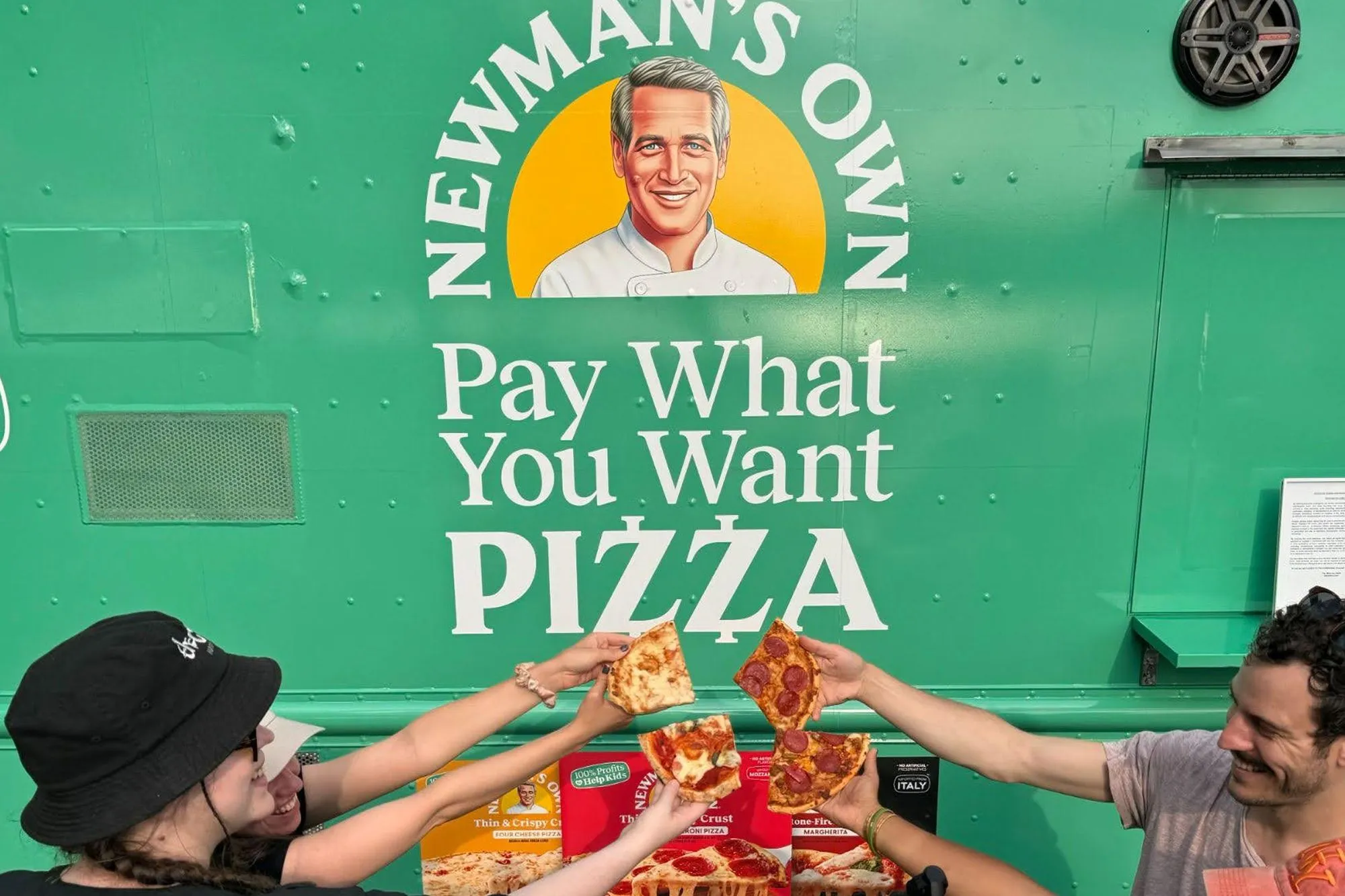 Guests clinking pizza slices together in front of a green Newman's Own pizza truck