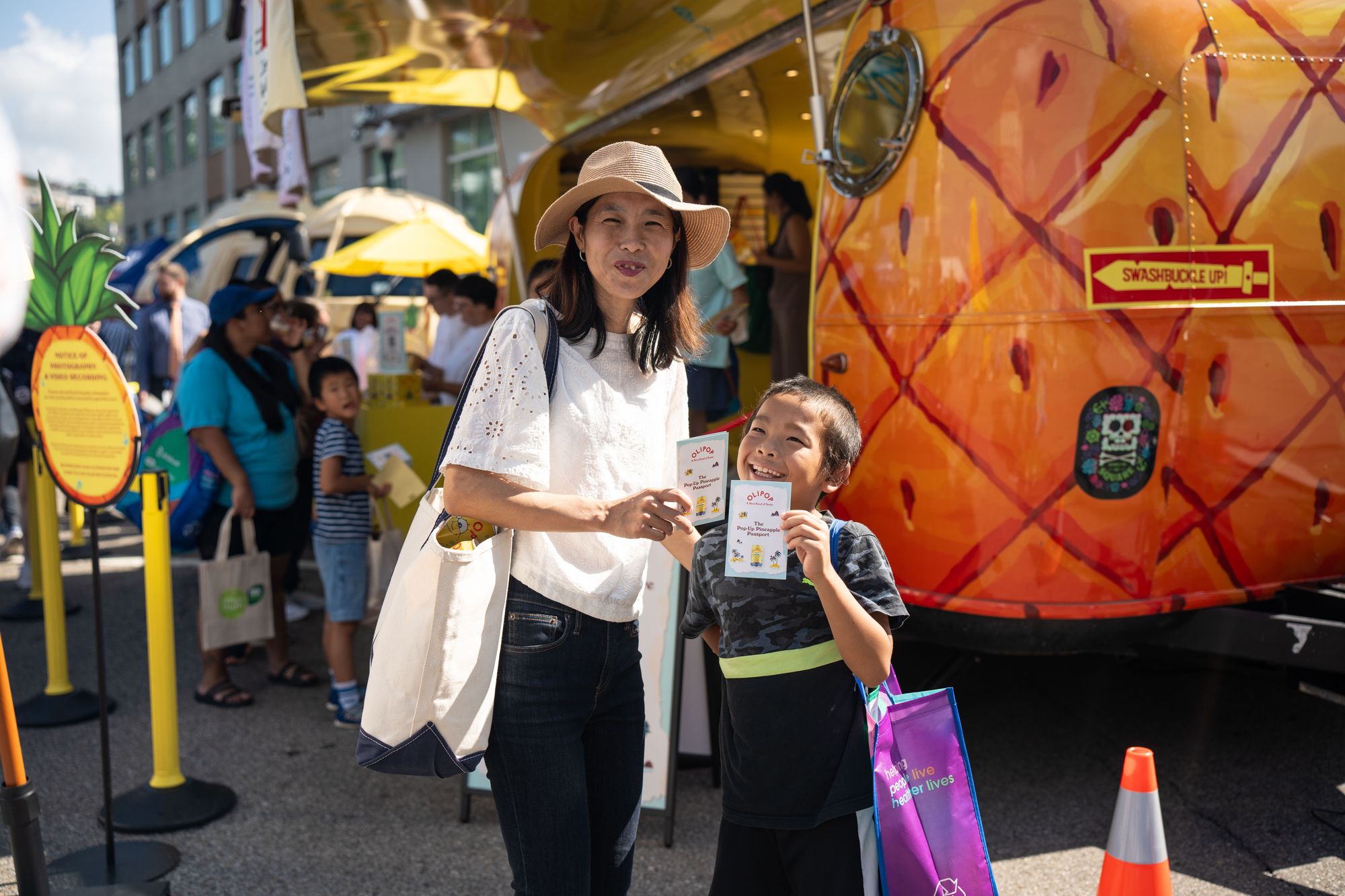Parent and child collecting samples at a pineapple shaped branded trailer