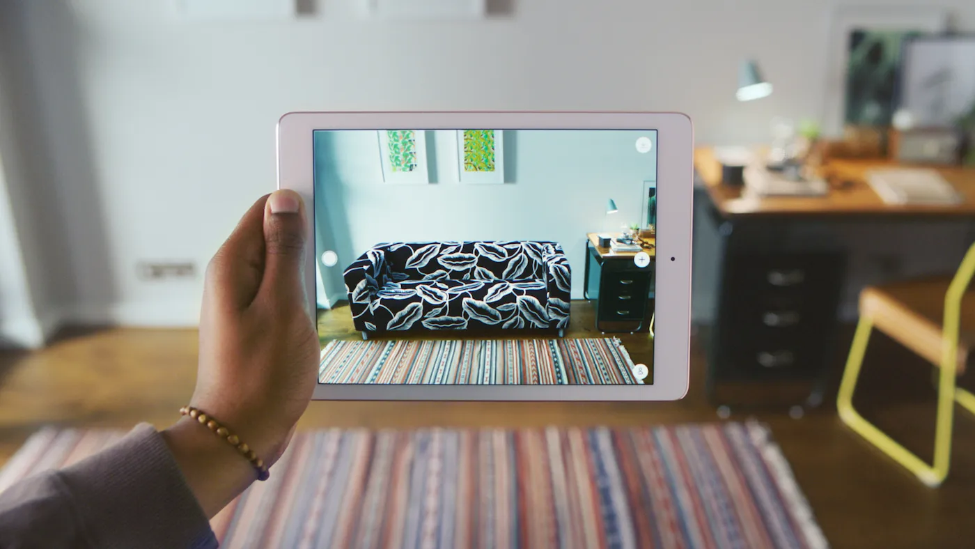 Person holding a tablet that overlays a virtual sofa into a real living room