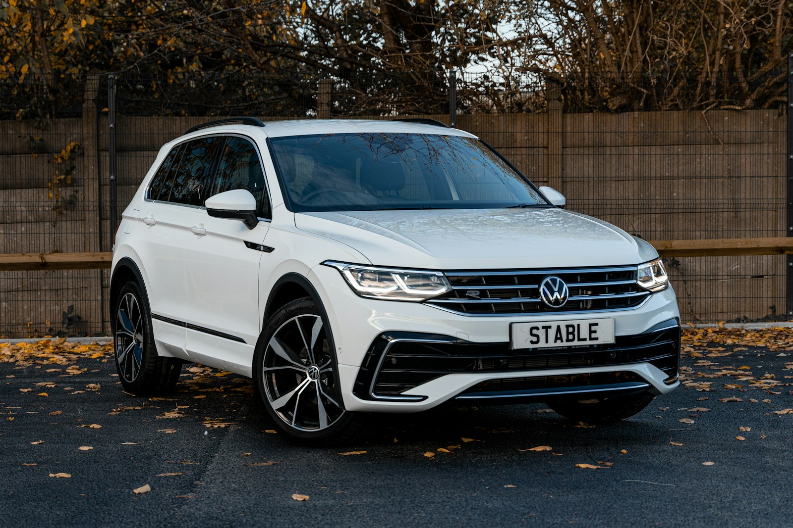 White Volkswagen Tiguan compact SUV parked on a road with autumn leaves, available for car hire in Spain
